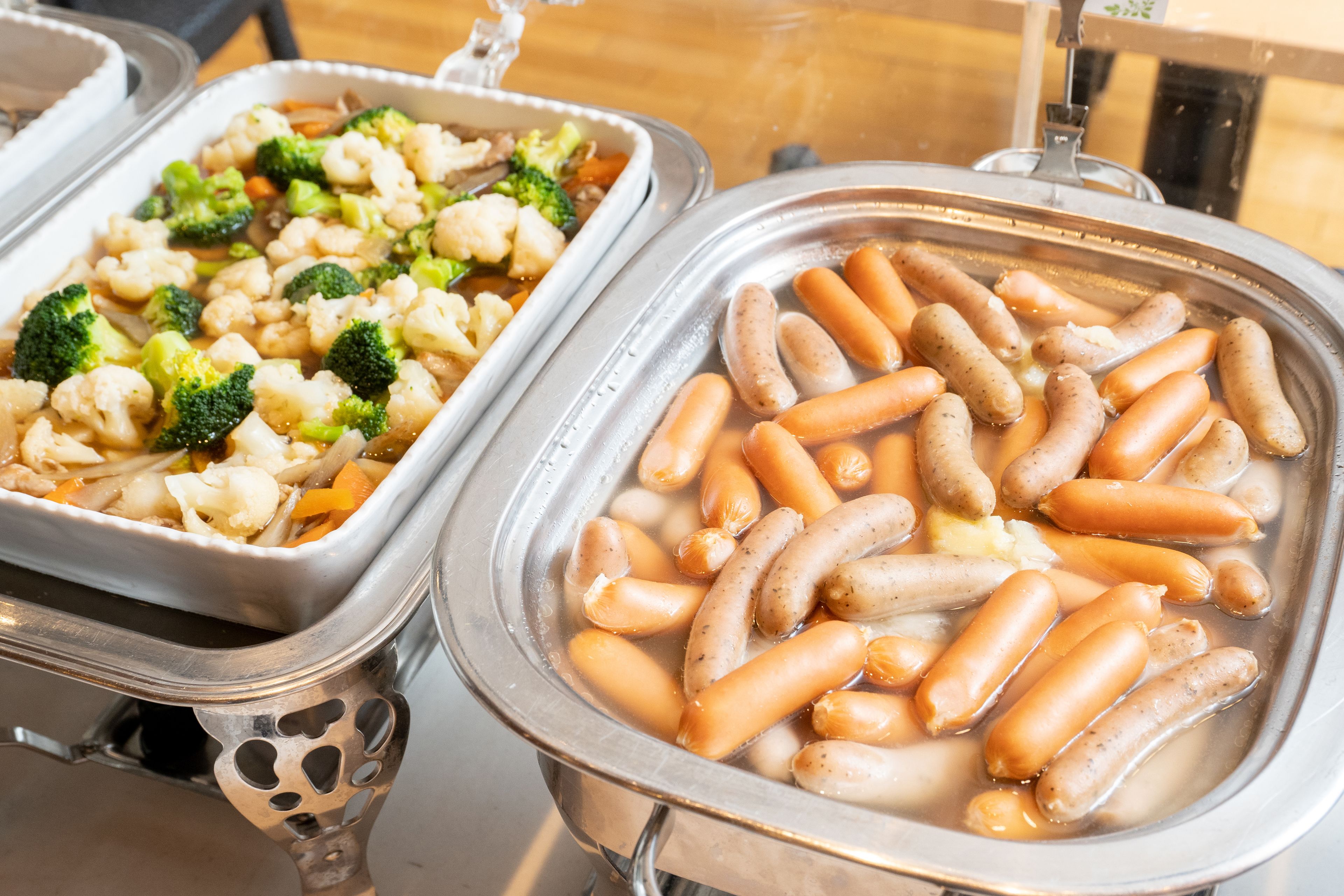 Dos dispensadores de comida con diversos platos, incluyendo salchichas y verduras.