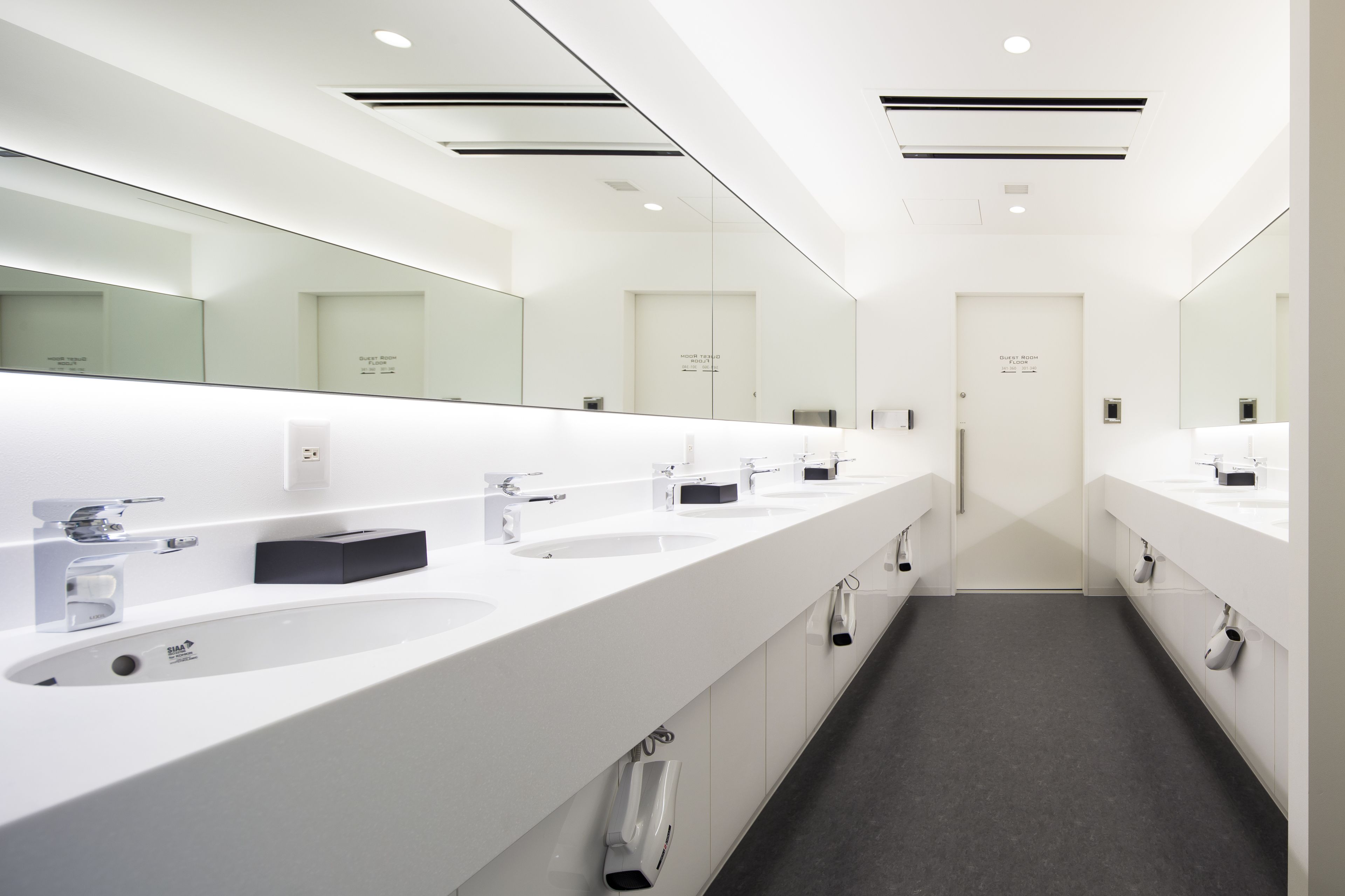A modern, well-lit public restroom with multiple sinks, mirrors, and a clean, minimalist design.