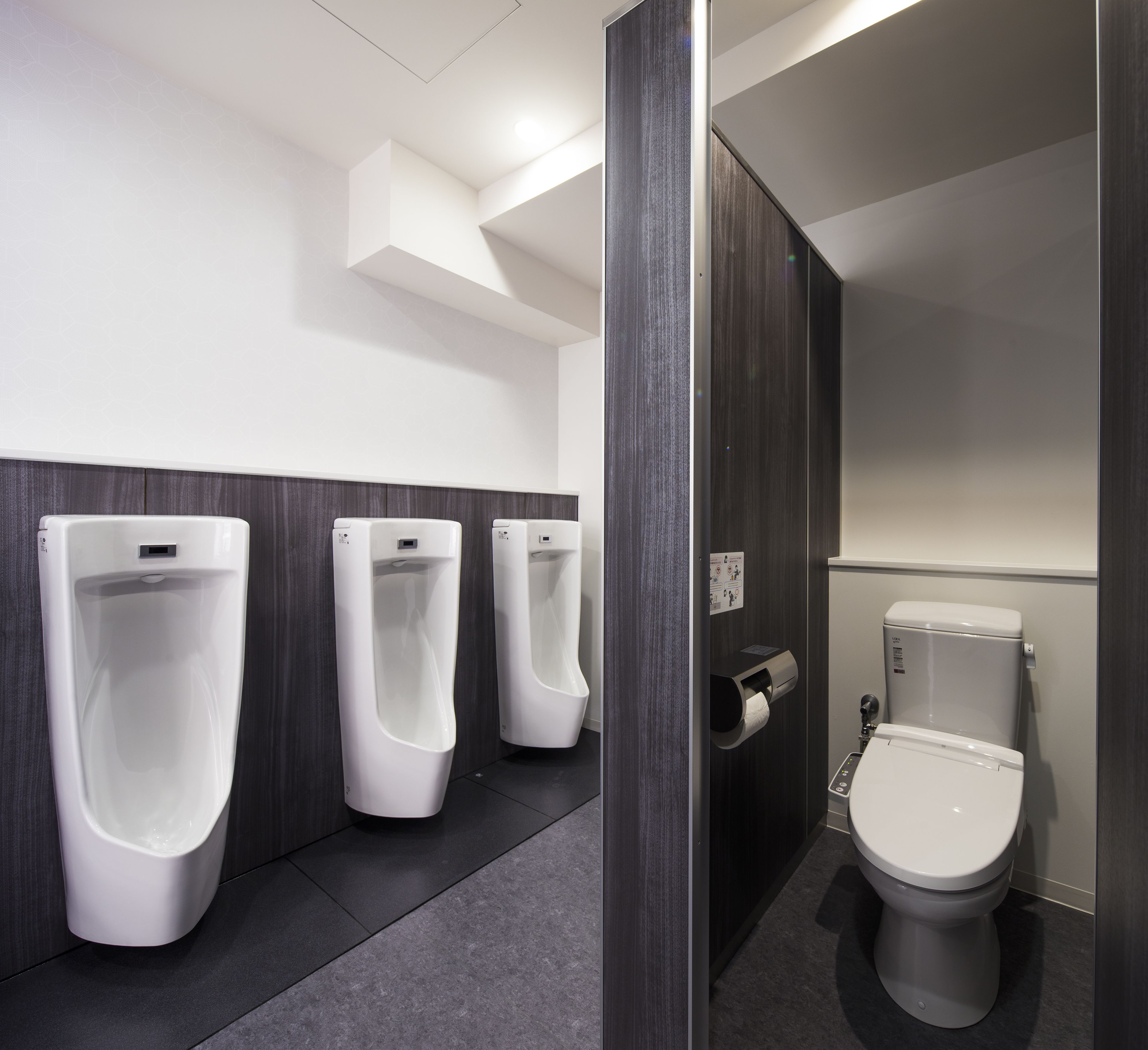 A men's restroom with three urinals, a toilet, and a paper towel dispenser.