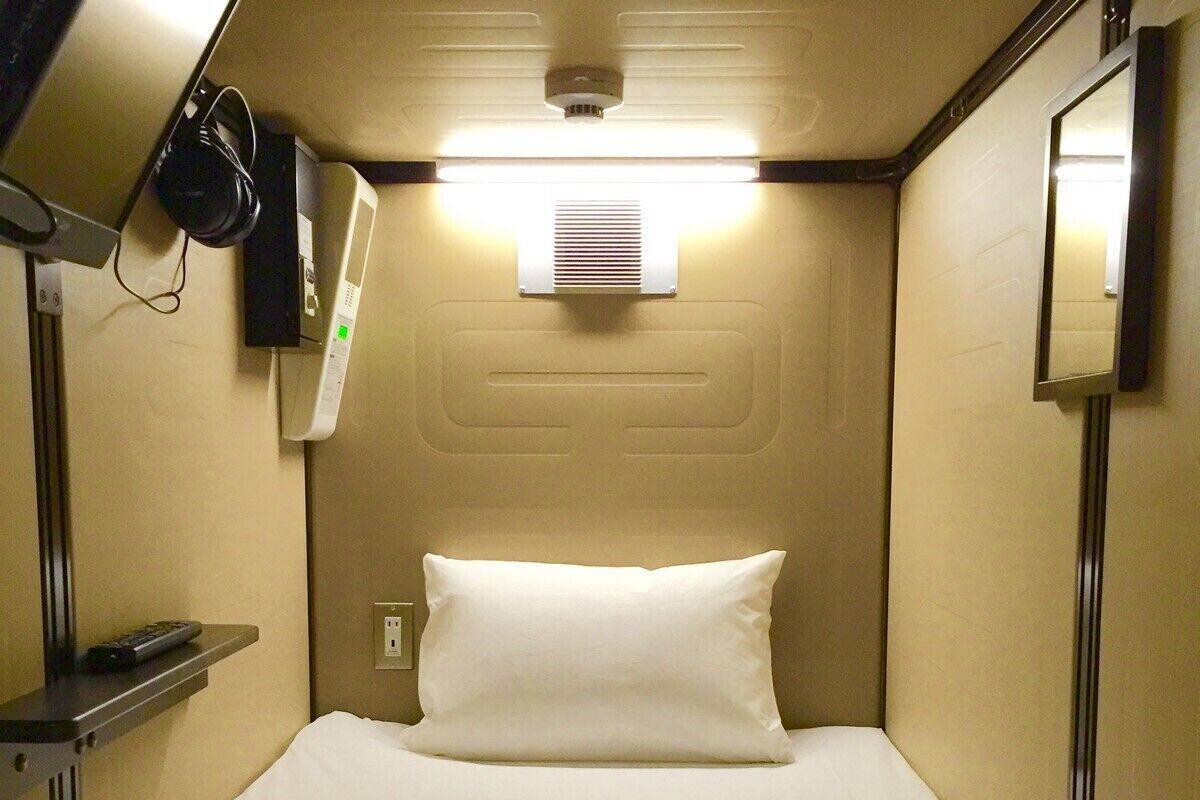A compact hotel room with a bed, a bedside table, a wall-mounted heater, and a mirror.