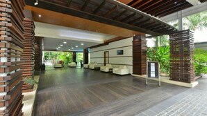 A spacious lobby with a modern design, featuring a wooden reception desk, seating area, and a view of the outdoors. - Elysium The Drift Apartment (Palm Cove)