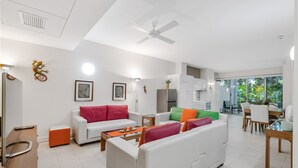 A modern living room with white sofas, a coffee table, and a dining area with wooden furniture. - Elysium The Drift Apartment (Palm Cove)
