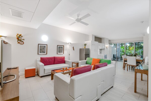 A modern living room with white sofas, a coffee table, and a dining area with wooden furniture.