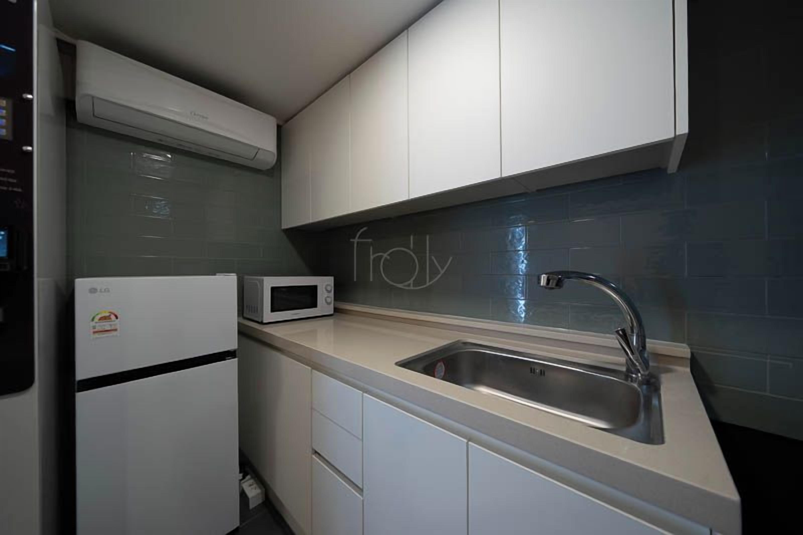 Una cocina compacta con microondas integrado, pileta de acero inoxidable y muebles blancos.