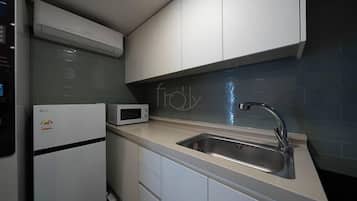 Una cocina compacta con microondas integrado, pileta de acero inoxidable y muebles blancos.