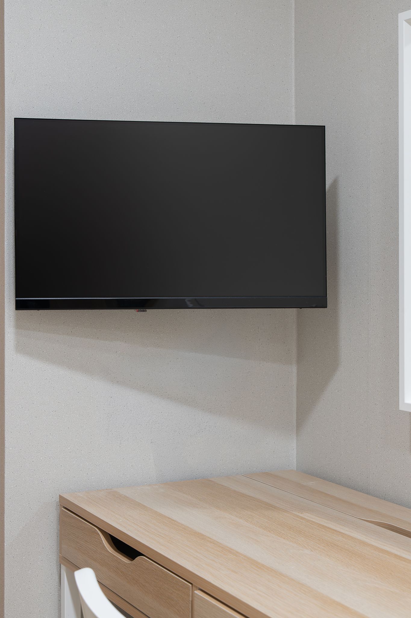 A flat-screen TV mounted on a wall above a wooden desk with drawers.