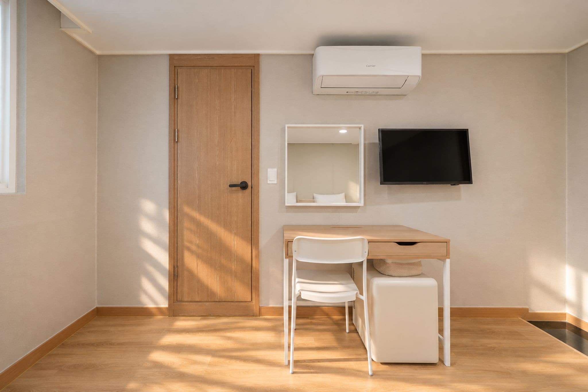 Una habitación con puerta de madera, un escritorio con silla, un radiador blanco y un televisor de pantalla plana montado en la pared.
