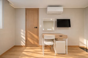 Una habitación con puerta de madera, un escritorio con silla, un radiador blanco y un televisor de pantalla plana montado en la pared.