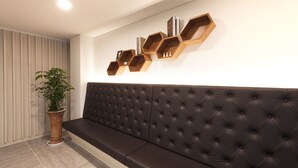 Un área de espera moderna con un banco tapizado marrón oscuro, estantes hexagonales de madera en la pared y una planta en maceta.