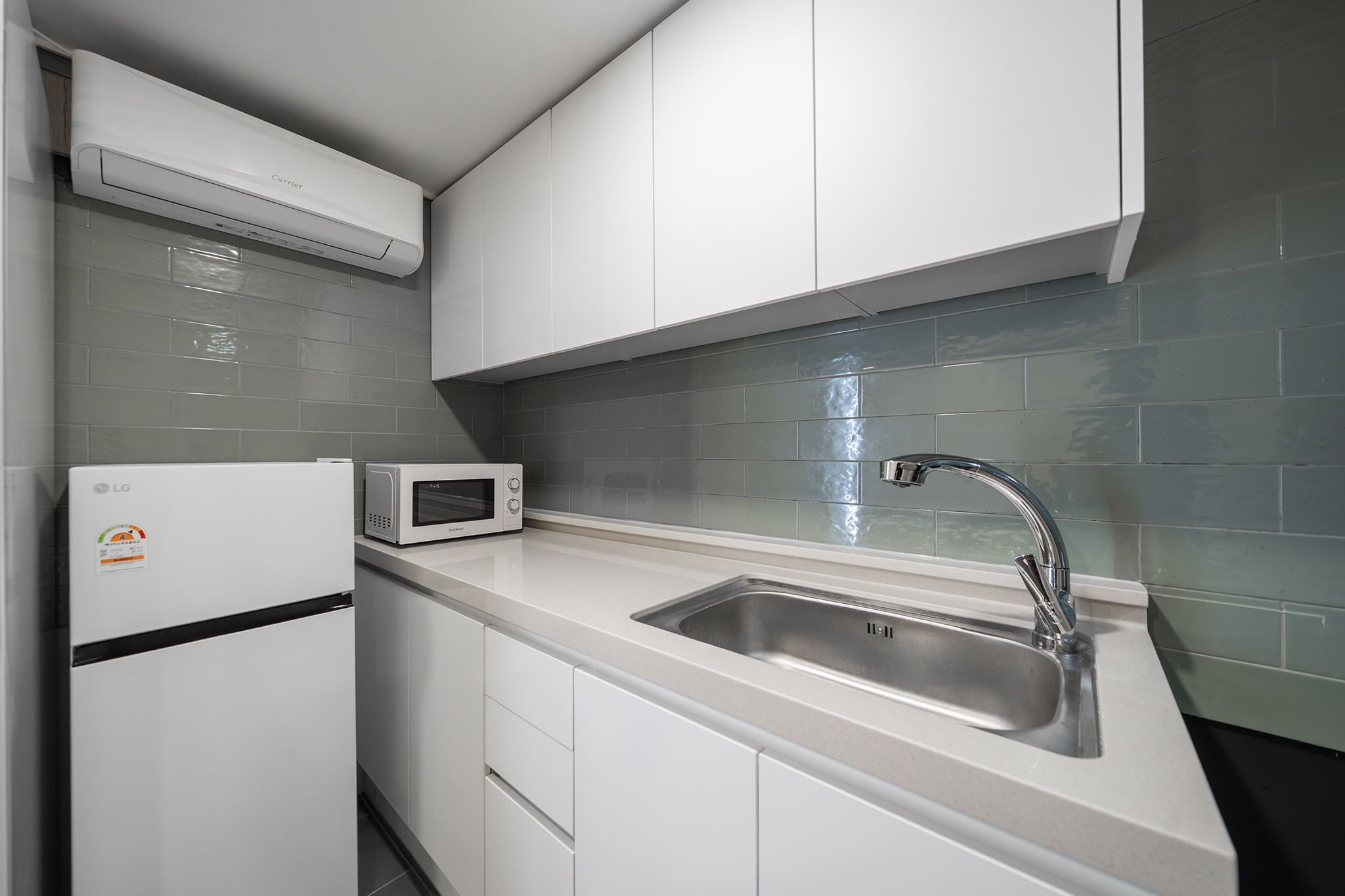 A modern kitchen with white cabinets, a stainless steel sink, a microwave, and an air conditioner.