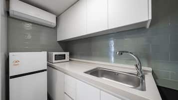 A modern kitchen with white cabinets, a stainless steel sink, a microwave, and an air conditioner.
