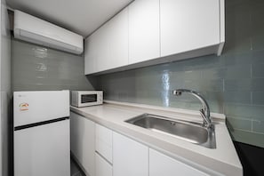 A modern kitchen with white cabinets, a stainless steel sink, a microwave, and an air conditioner.