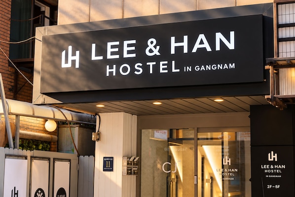 A hostel sign with the name 'LEE & HAN HOSTEL IN GANGNAM' and a door with a glass panel.