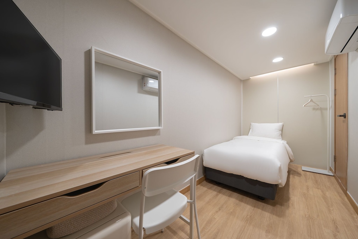 A hotel room with a bed, a desk, a chair, a television, and a wardrobe.