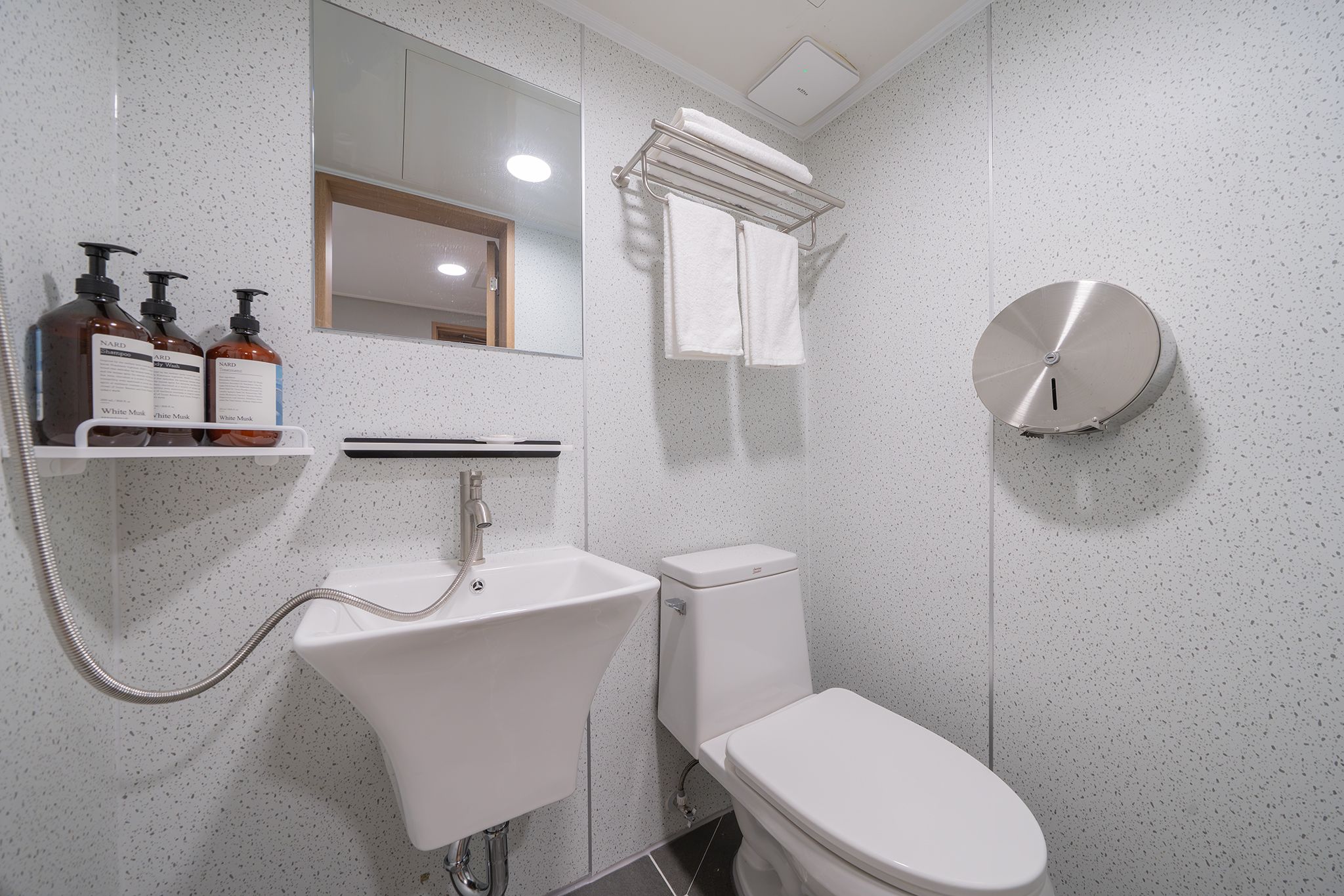 A modern bathroom with a white sink, a toilet, and a shower. There is a mirror above the sink and a towel rack above the toilet.