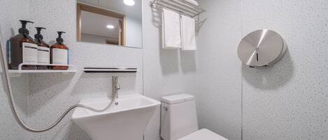 A modern bathroom with a white sink, a toilet, and a shower. There is a mirror above the sink and a towel rack above the toilet.