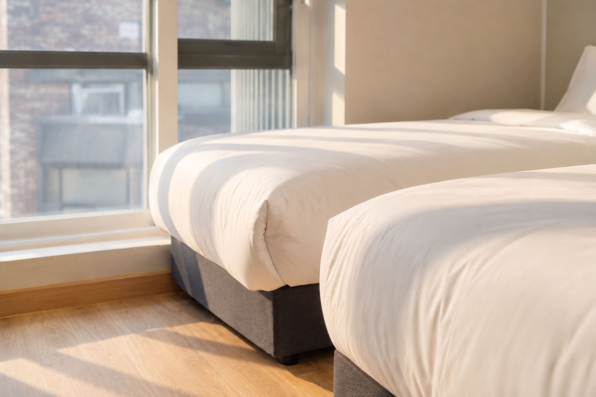 A bedroom with two beds, a window, and a view of buildings.