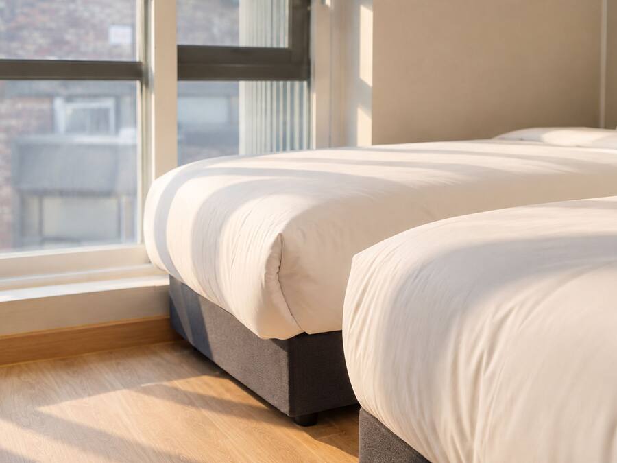 Un dormitorio con dos camas, una ventana y vistas a edificios.