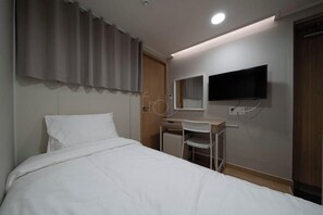 Una habitación de hotel con una cama, un escritorio con una silla, un televisor y una puerta.