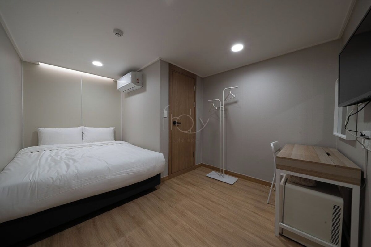 Un dormitorio con cama, armario, mesita de noche, lámpara de pie y televisor.