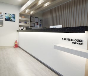 Una recepción con el rótulo "K-GUESTHOUSE PREMIUM", diseño moderno, un extintor y certificados enmarcados en la pared.