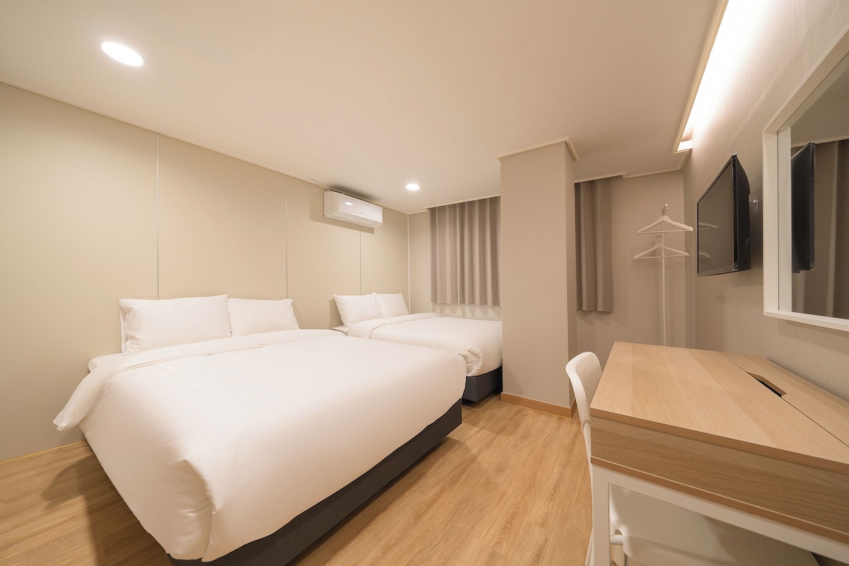 A hotel room with two beds, a wooden desk, a mirror, and a television.