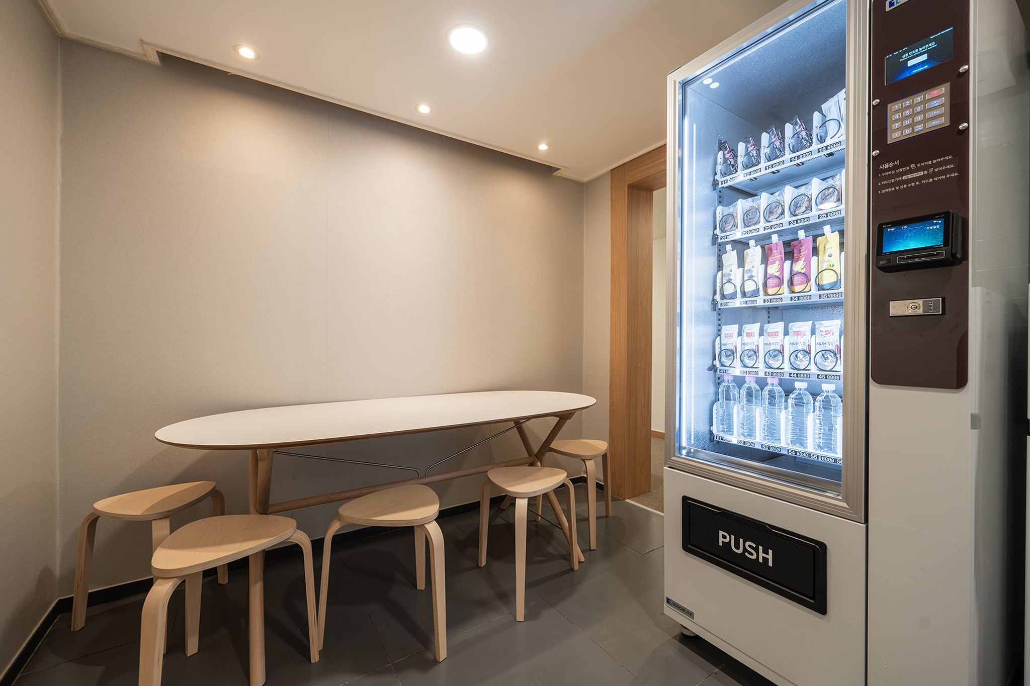 A room with a table and four stools, a vending machine with a 'PUSH' button, and a window with a view of a building.