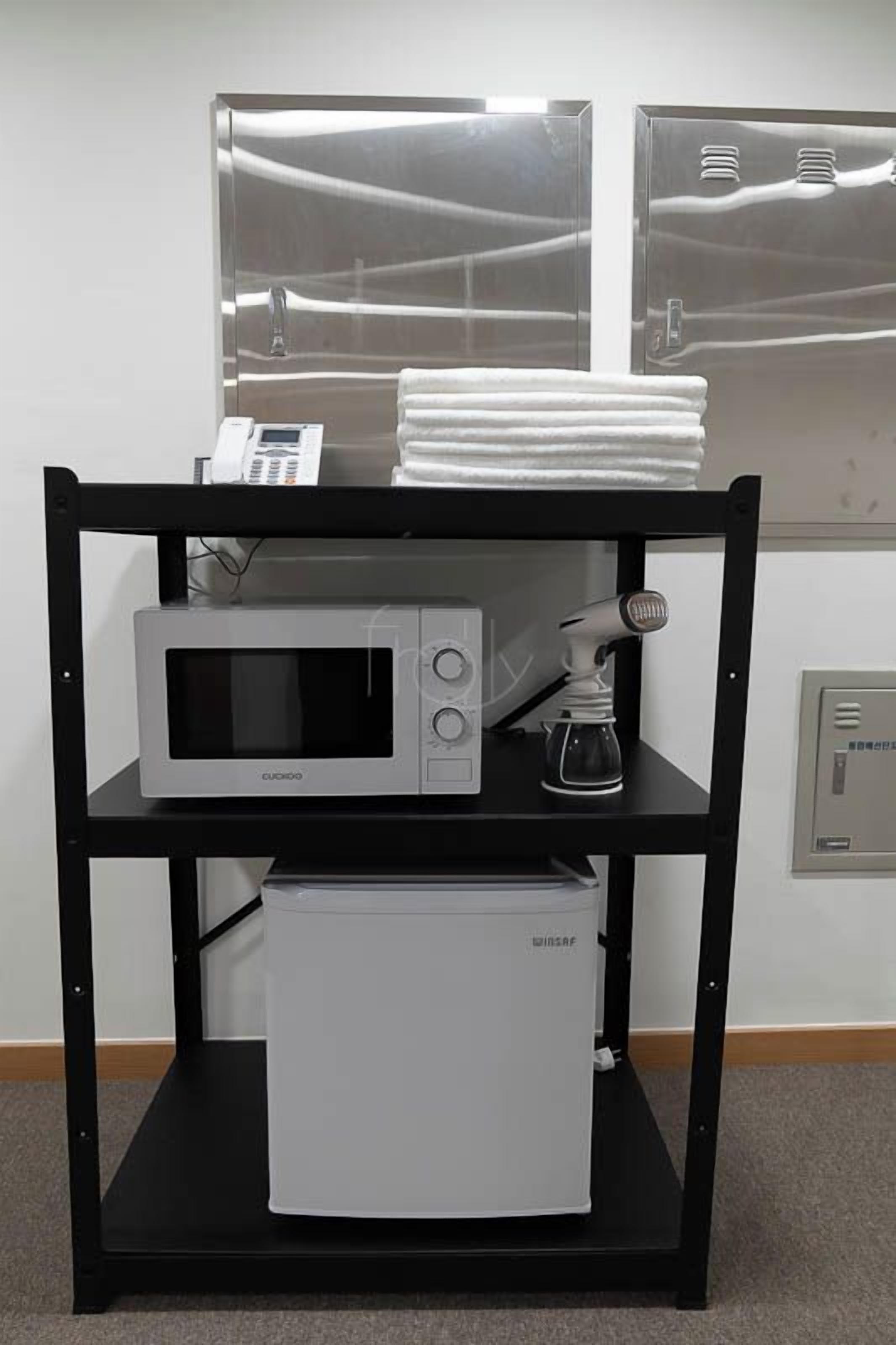 Una kitchenette con microondas, cafetera y un refrigerador pequeño sobre un soporte de metal negro.