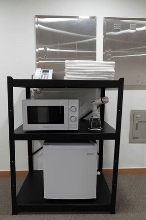 Una kitchenette con microondas, cafetera y un refrigerador pequeño sobre un soporte de metal negro.