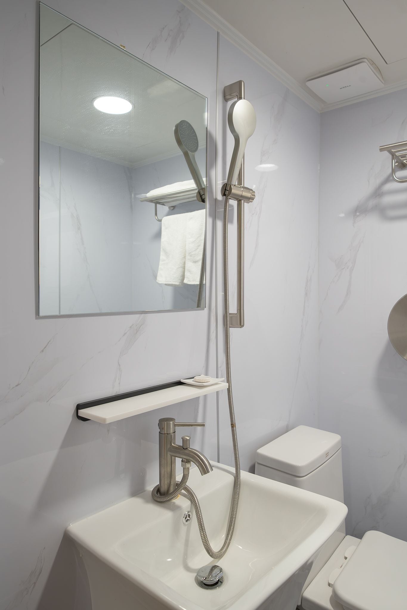 Un baño moderno con un lavamanos blanco, un espejo, un cabezal de ducha manual y un inodoro.