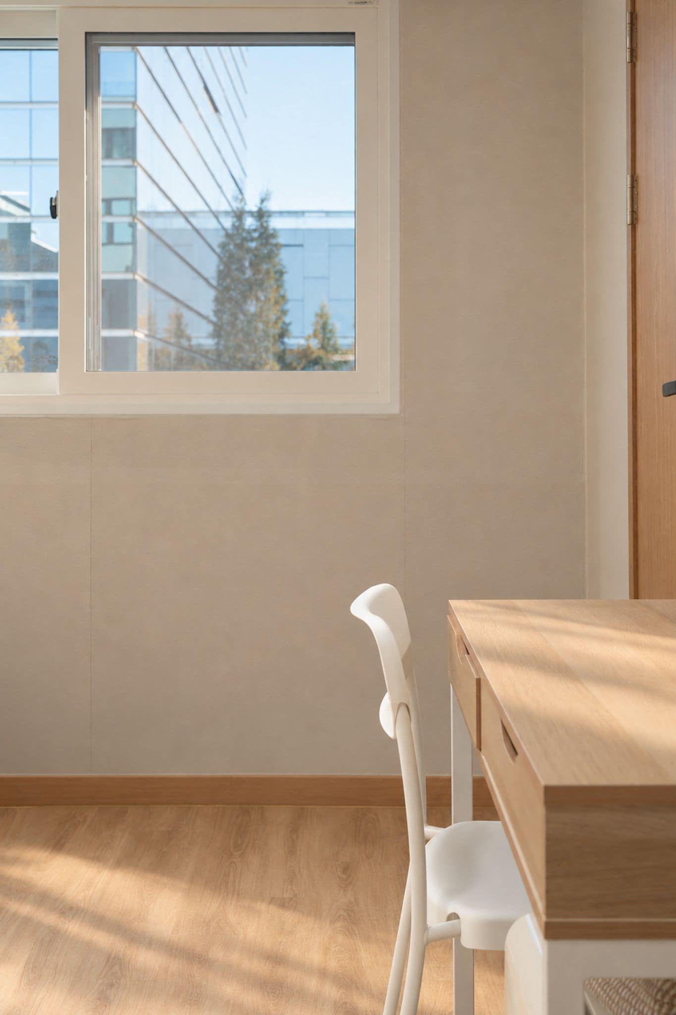 A room with a window, a wooden desk, and a white chair.