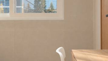 A room with a window, a wooden desk, and a white chair.