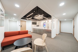 A modern office space with a reception desk, a seating area with a sofa and chairs, and a kitchenette.
