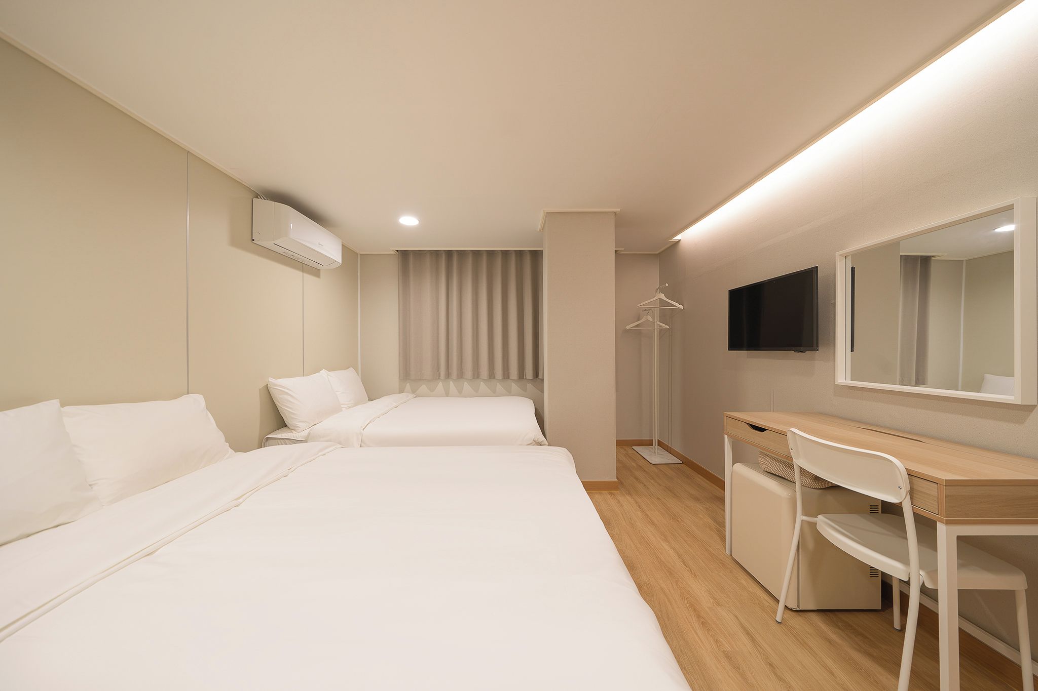 A hotel room with two beds, a desk, a chair, a TV, and a wardrobe.