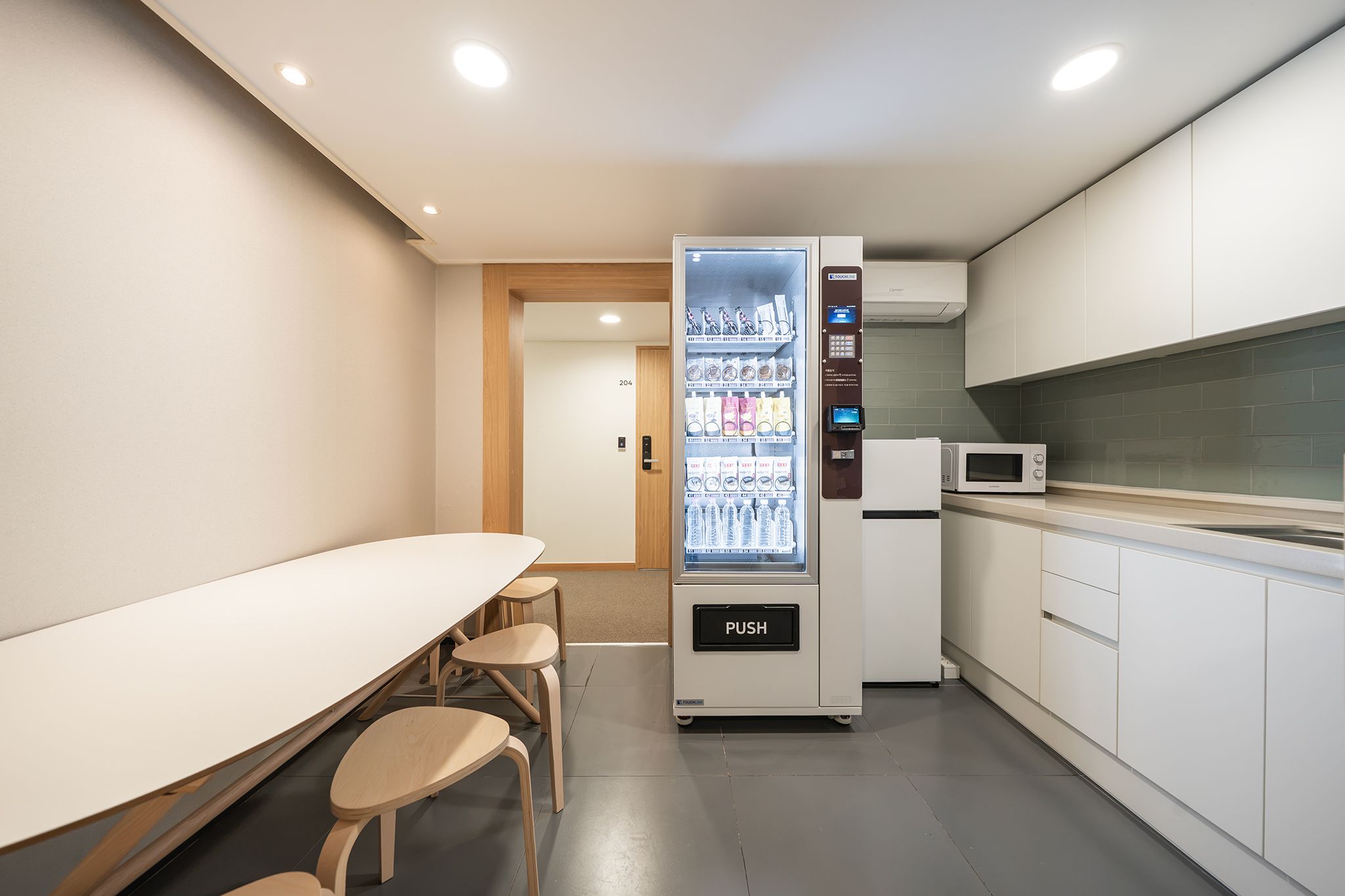 A modern kitchenette with a microwave, a refrigerator, and a vending machine.