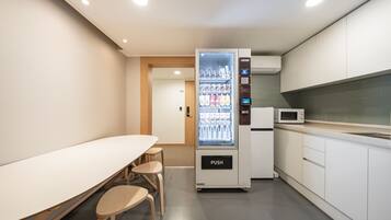 A modern kitchenette with a microwave, a refrigerator, and a vending machine.