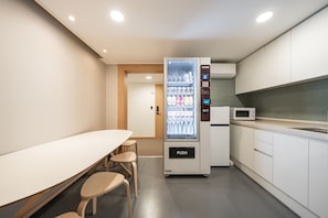 A modern kitchenette with a microwave, a refrigerator, and a vending machine.