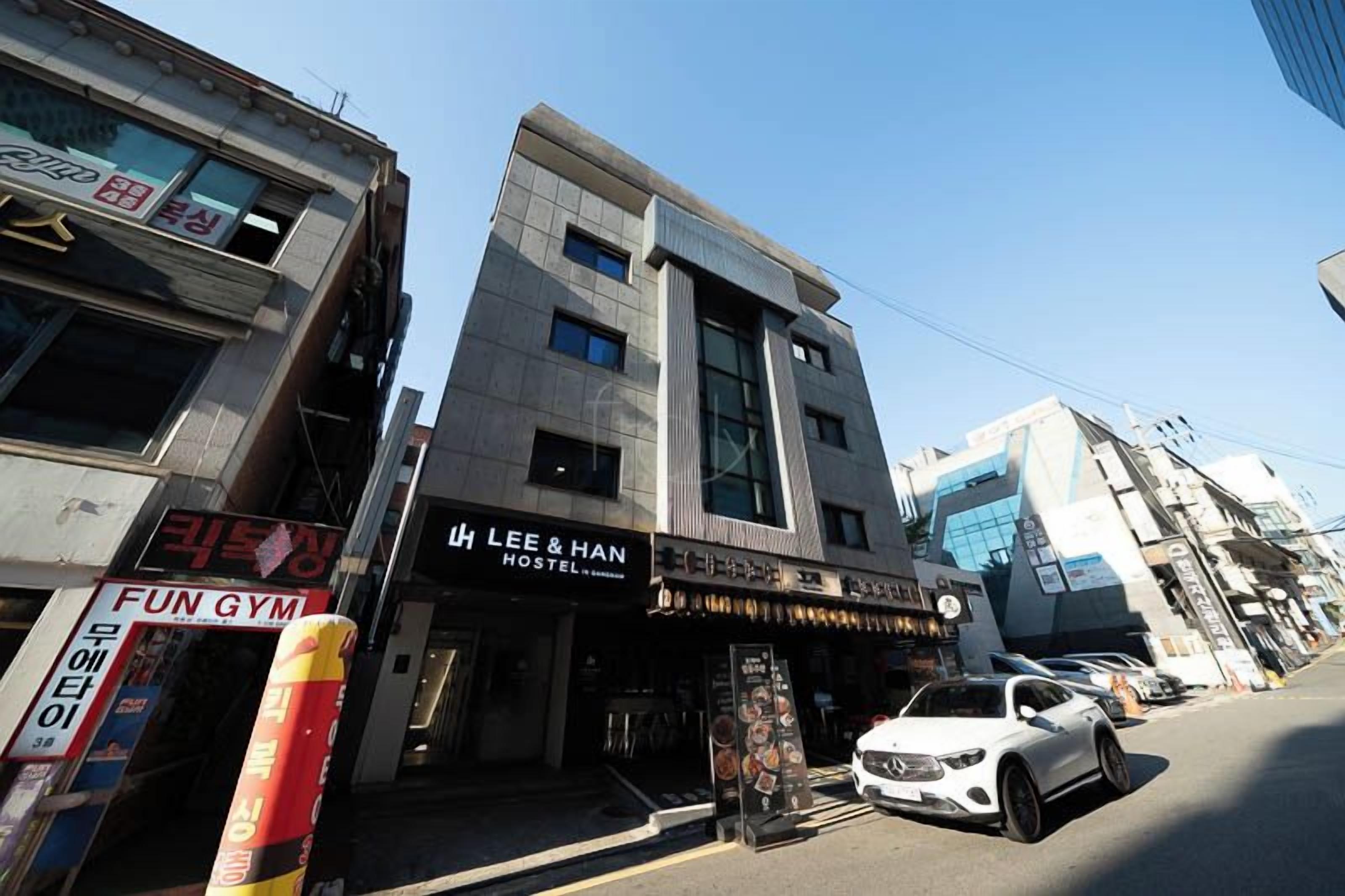 Un edificio de varios pisos con un letrero que dice 'LEE & HAN HOSTEL' y 'FUN GYM' en la planta baja.