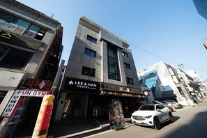 Un edificio de varios pisos con un letrero que dice 'LEE & HAN HOSTEL' y 'FUN GYM' en la planta baja.