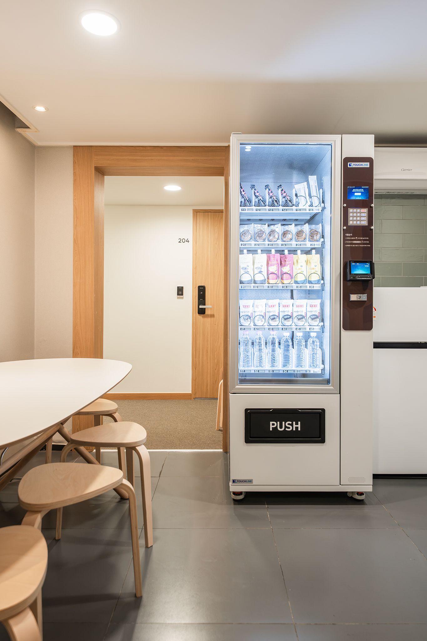 A vending machine with a push button, located in a room with a table and chairs.