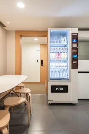 A vending machine with a push button, located in a room with a table and chairs.