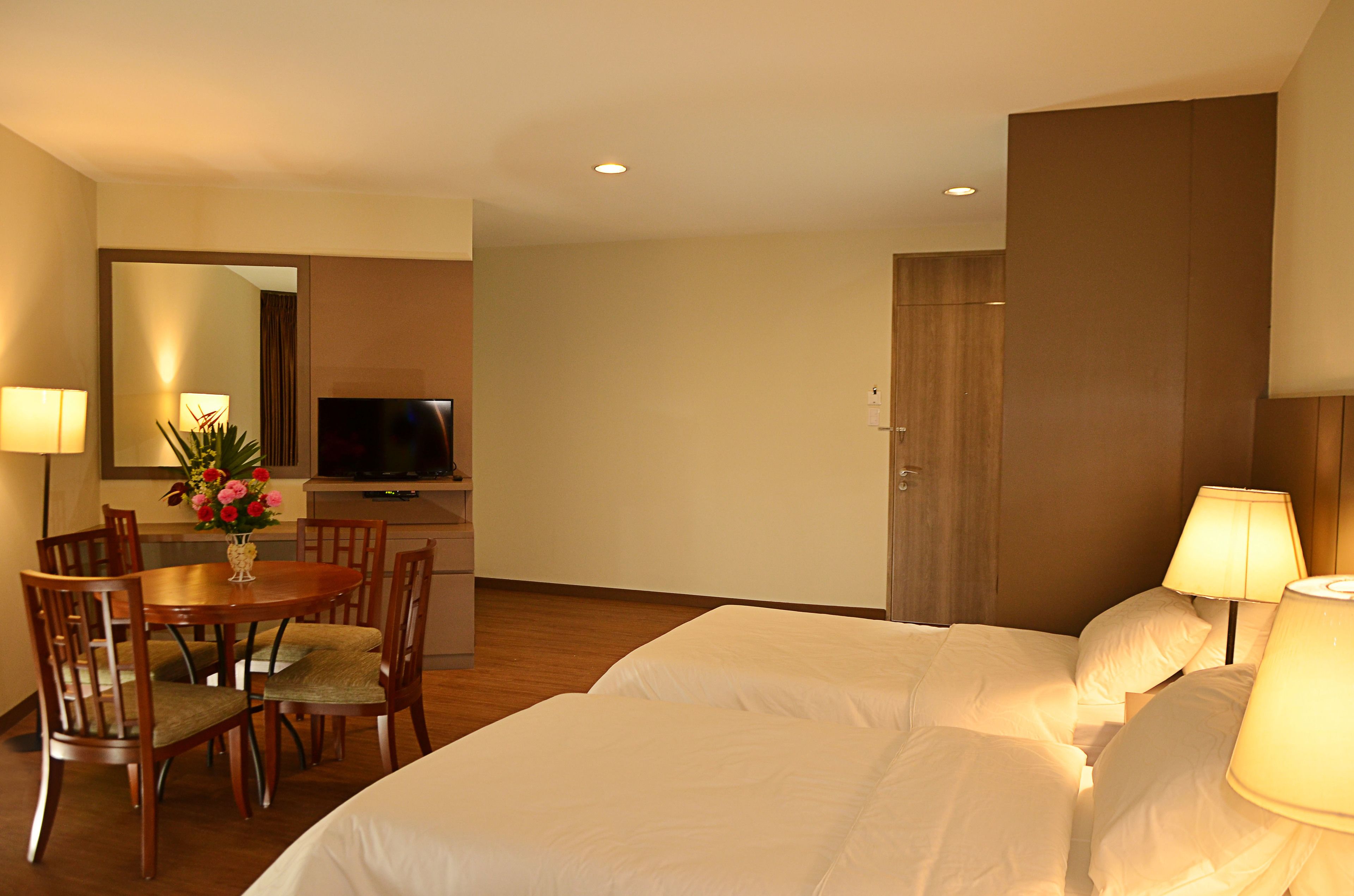 A hotel room with two beds, a dining table with chairs, a TV, and a mirror.