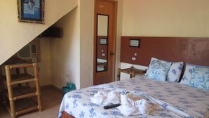 Habitación de hotel con cama, una silla de madera, una mesita y un espejo en la pared.