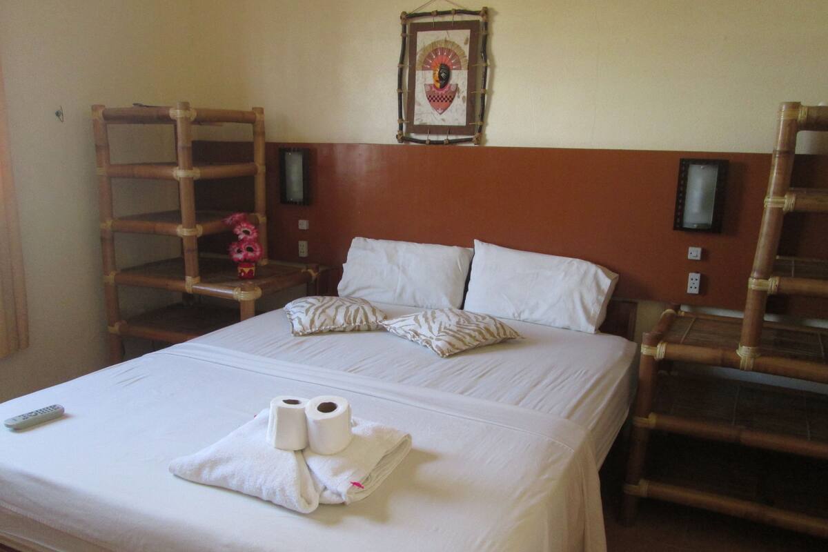 A hotel room with a large bed, two nightstands, a wooden headboard, a framed picture on the wall, and a remote control on the bed.