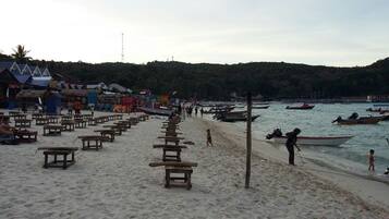 A beach with wooden benches, boats, and a few people.