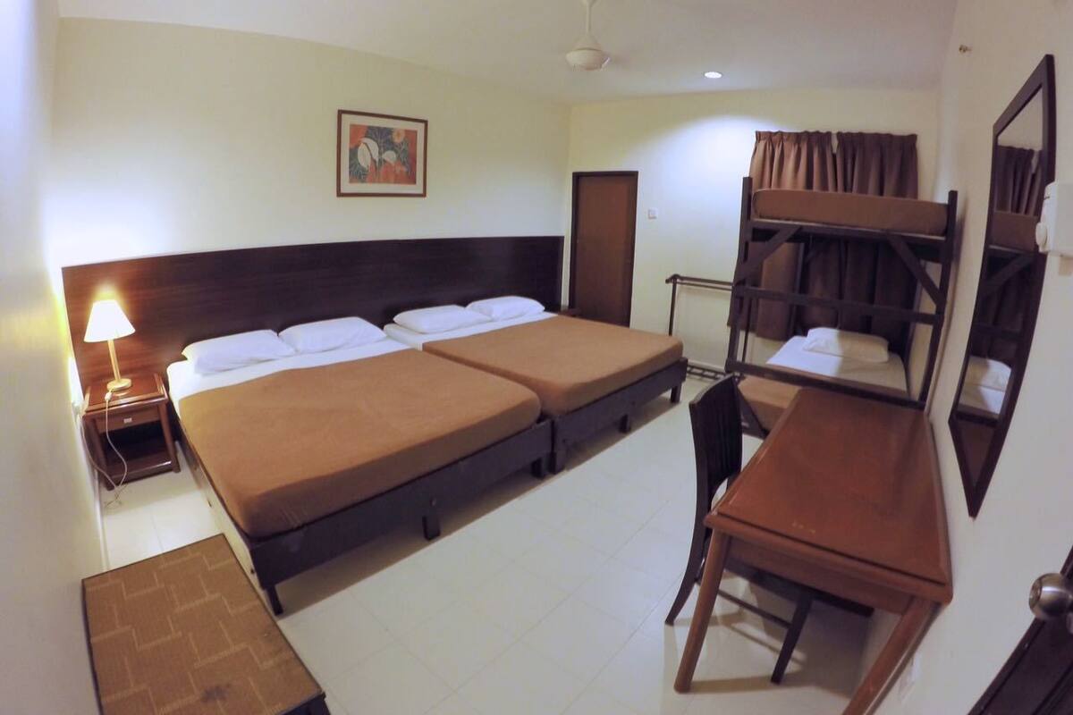 Ein Hotelzimmer mit zwei Einzelbetten, einem Schreibtisch, einem Stuhl, einem Spiegel und einem Deckenventilator.