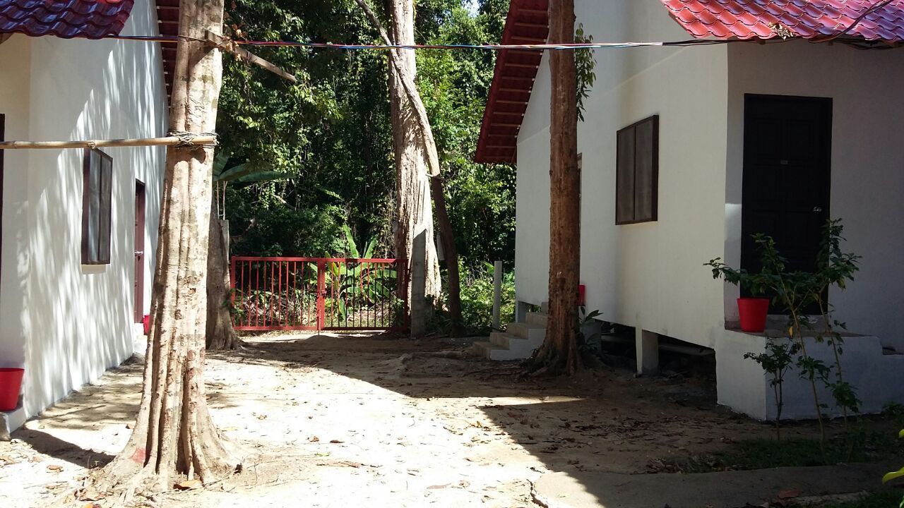 A courtyard with a red gate, trees, and a white building with a red roof.