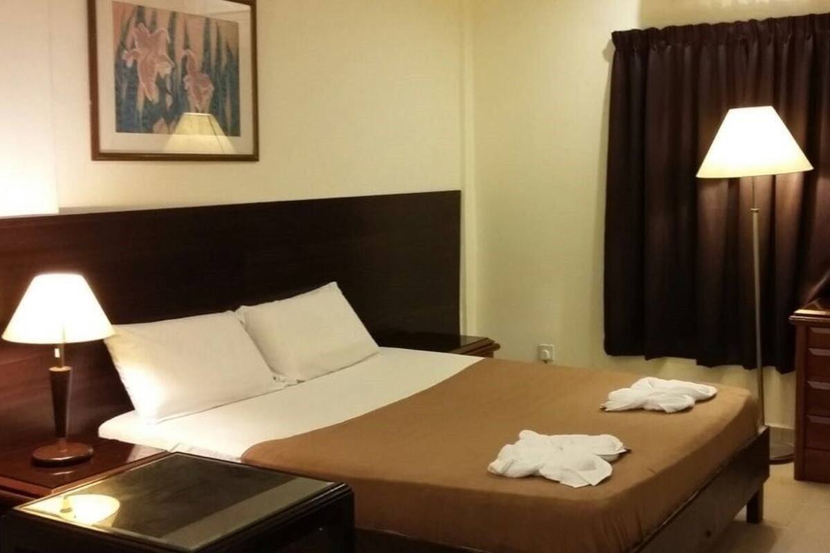 Ein Hotelzimmer mit einem Bett, zwei Nachttischlampen, einem Schreibtisch mit Stuhl, einem Spiegel und einem Bild an der Wand.