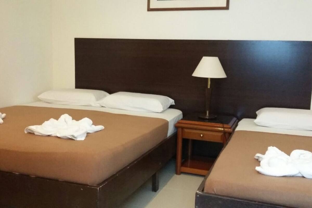 Ein Hotelzimmer mit zwei Einzelbetten, einem Nachttisch mit Lampe und einem Holz-Kopfteil.
