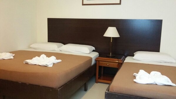 Habitación de hotel con dos camas individuales, una mesita de noche con lámpara y un cabecero de madera.